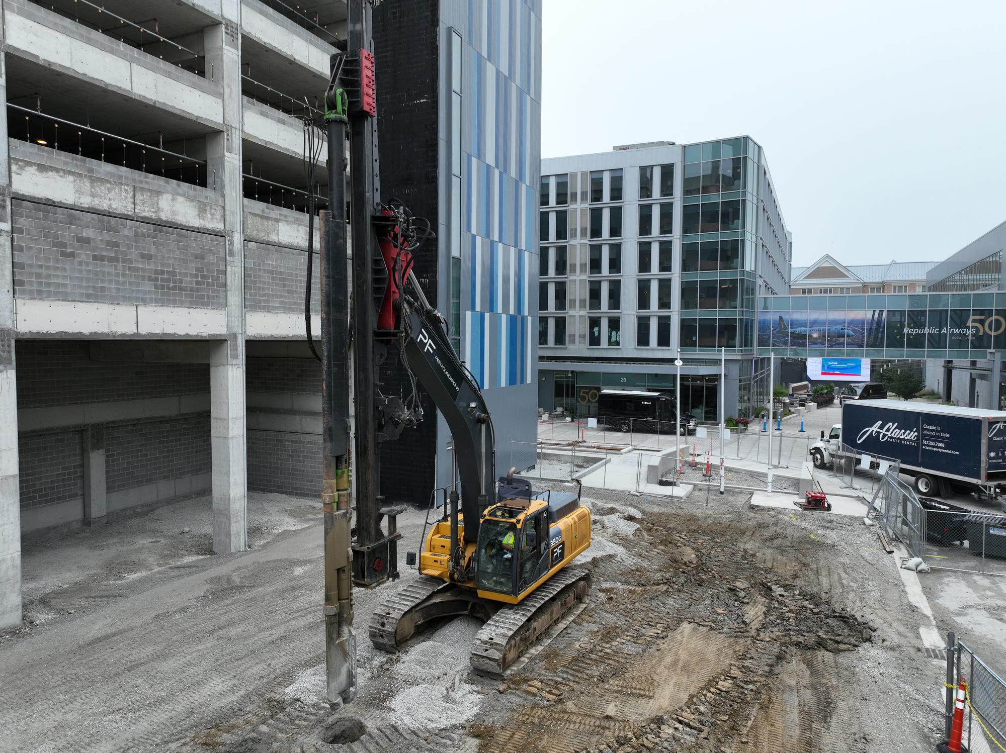 Pier Foundations' PF-branded drilling rig installing aggregate piers beside a multi-story parking structure on the Republic Hotel Addition site in Carmel, Indiana.